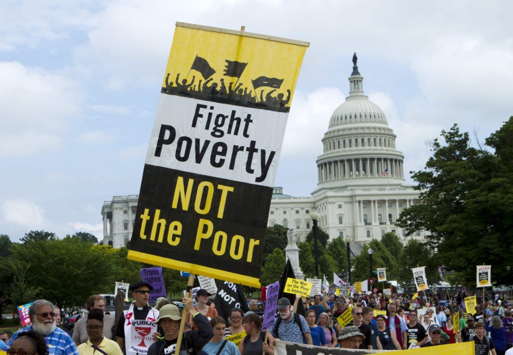 A crowd of protesters holding banners that read 'Fight Poverty NOT the Poor' in front of a government building, likely the Capitol, during a demonstration advocating against poverty.
